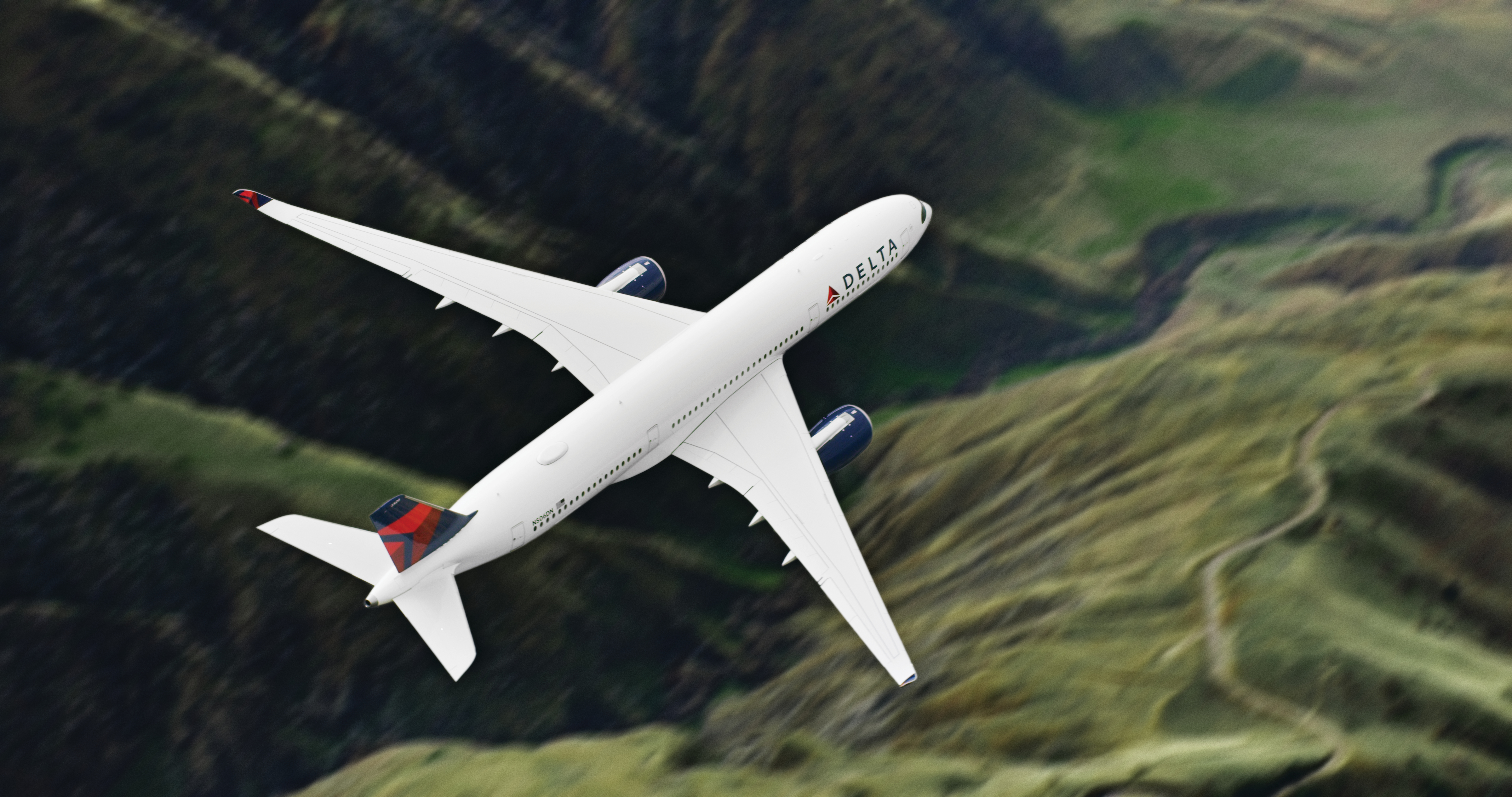Airbus A359-900 flies over green mountains