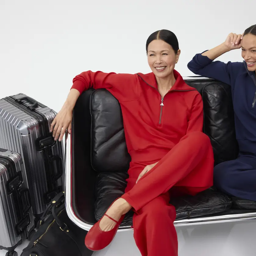 Two smiling women, sitting next to each other dressed in red and navy Spanx outfits.