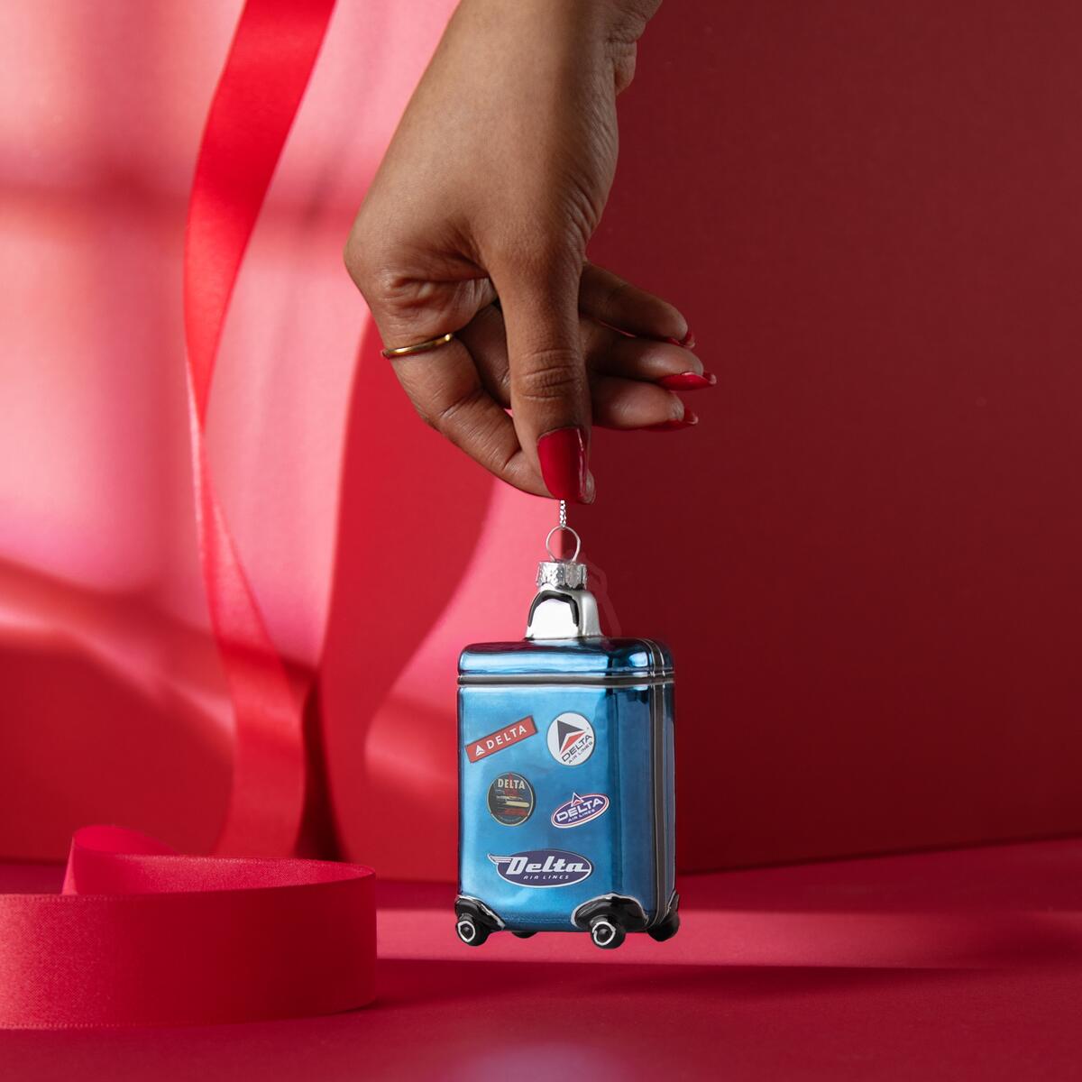 Roll into the holidays with our glass, Heritage Delta Suitcase ornament. This ornament is guaranteed to standout on your tree with its blue hues and miniature Heritage patches.  