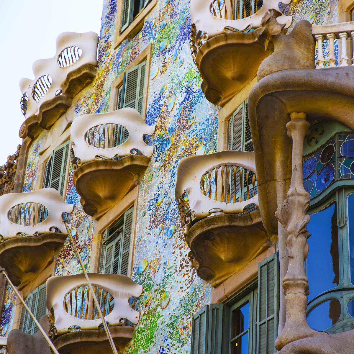 Colorful, organic-shaped balconies and windows on a decorative, mosaic-covered building façade.