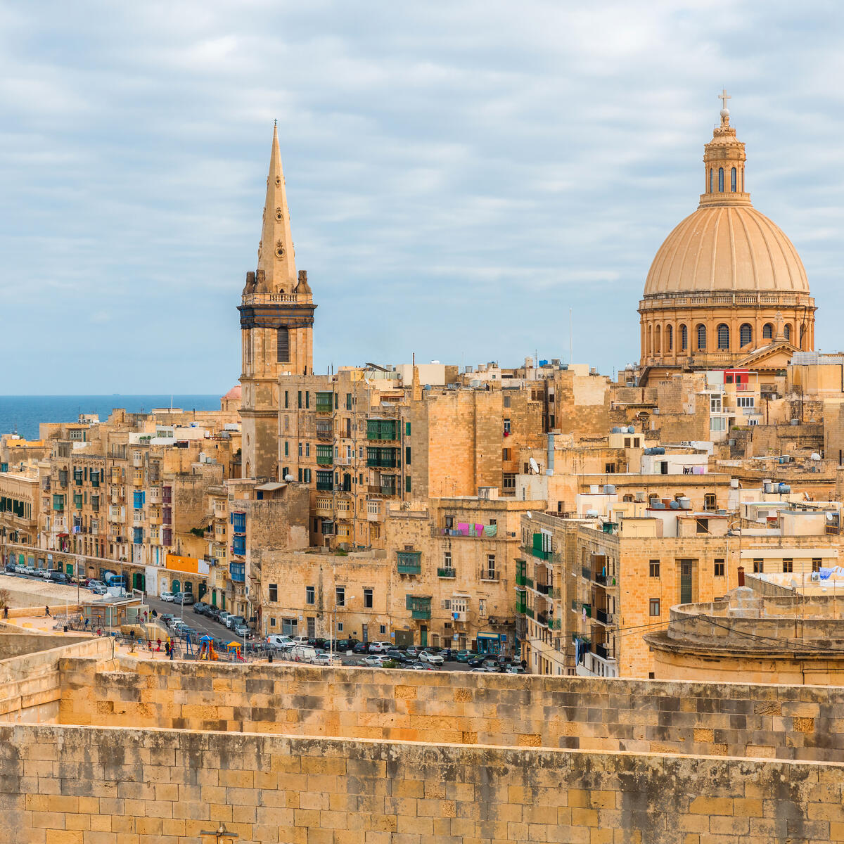 Historic limestone city with a large domed church and spire overlooking the sea.