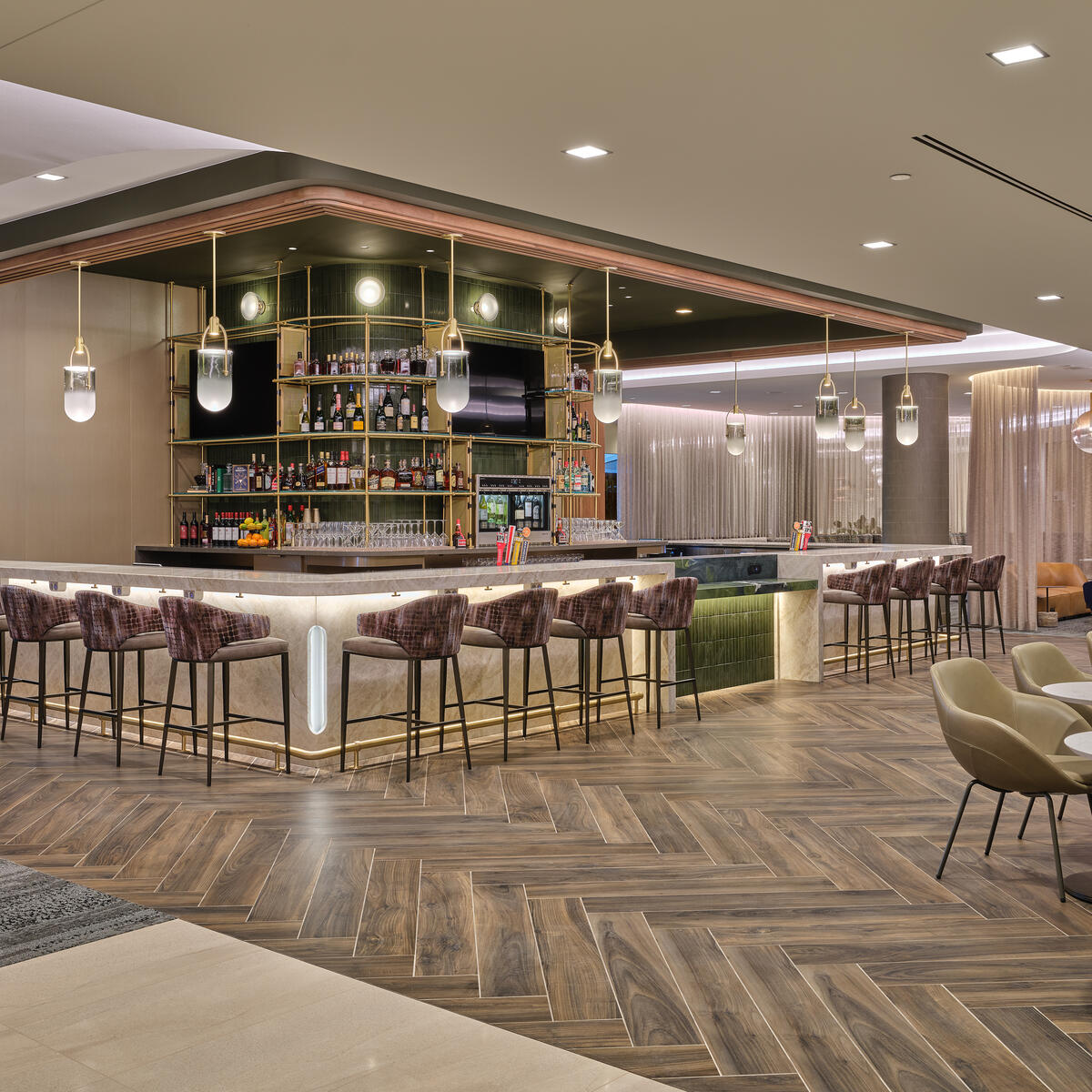 Lounge bar with high‑back stools, illuminated shelving, warm lighting and adjacent seating areas with small tables