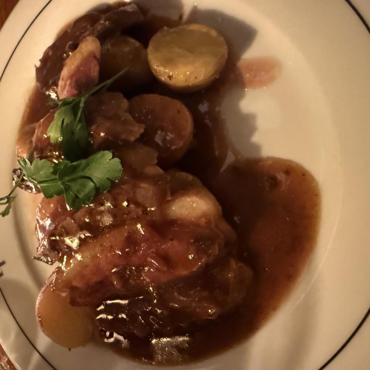 A white plate with a black rim holds a generous serving of sliced roasted meat and small potatoes, all covered in rich brown gravy and garnished with fresh parsley. The name "LA MARINE" is printed on the rim.