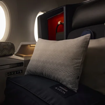 Delta One suite featuring premium bedding, pillows and an amenity kit by the window.