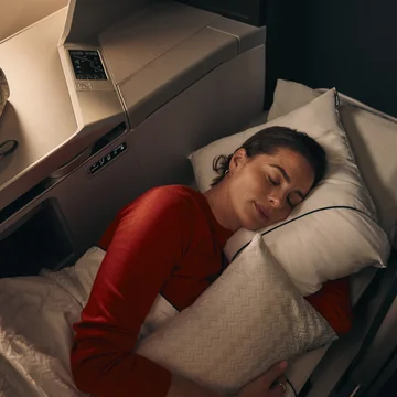 Customer resting in a lie-flat Delta One suite with bedding and pillow.