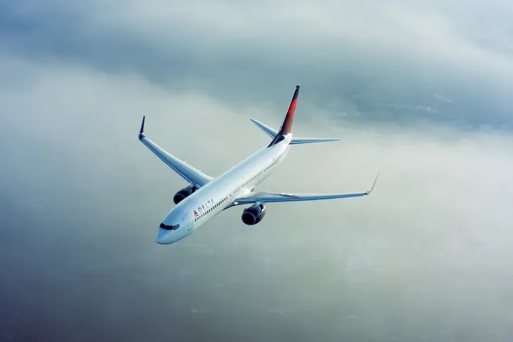 A 737-900 flies through clouds with a cityscape underneath.