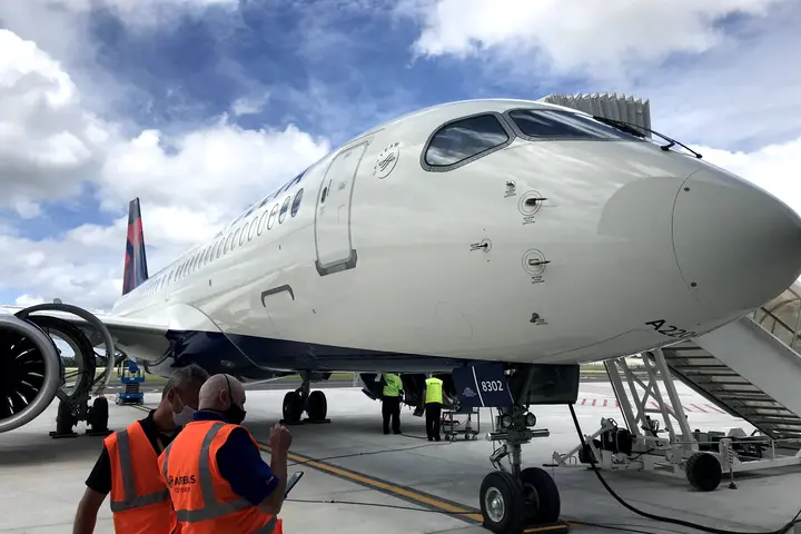 A220-300 parked on tarmac with stair truck and employees