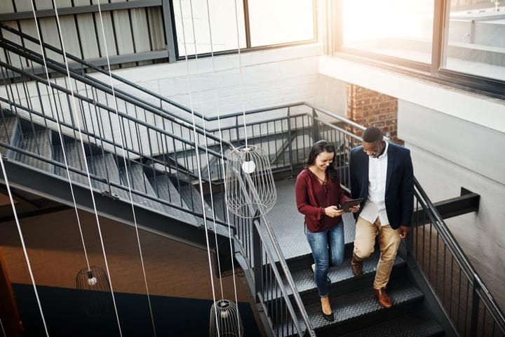 Two people walking down a flight of stairs looking at a tablet.