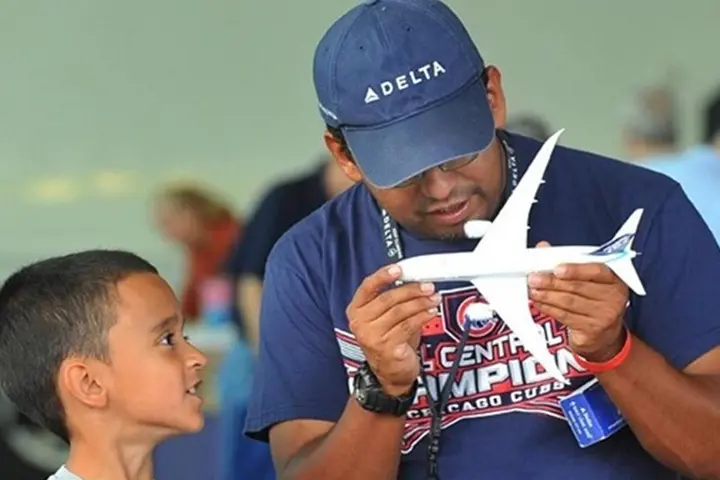 Man holds model airplane while boy looks on.