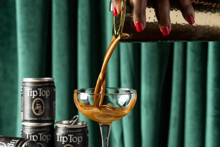 A hand pouring Tip Top Proper Cocktails' Espresso Martini into a martini glass.