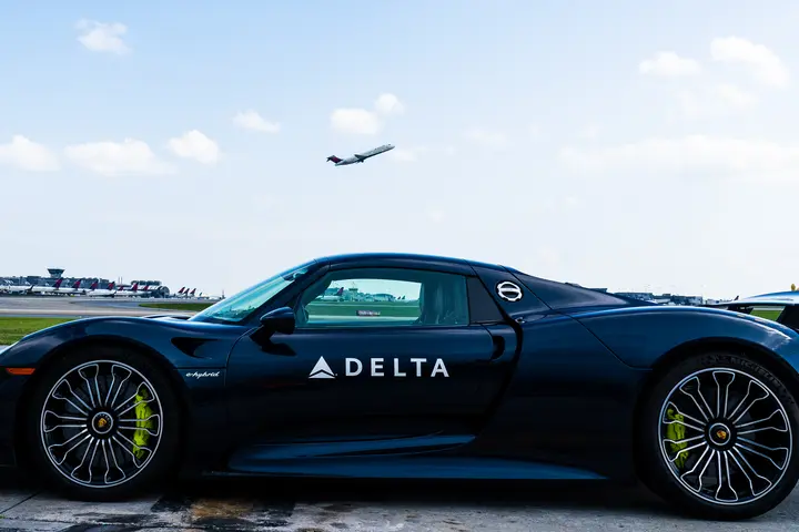 A Delta Boeing 717 takes off above a Porsche 918 Spyder at Hartsfield-Jackson Atlanta International Airport.