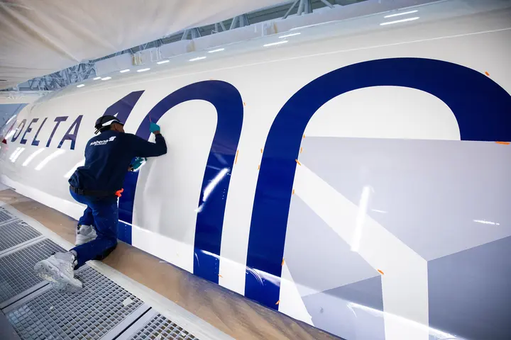 A bold 100 emblem is being painted on the side of a Delta aircraft.
