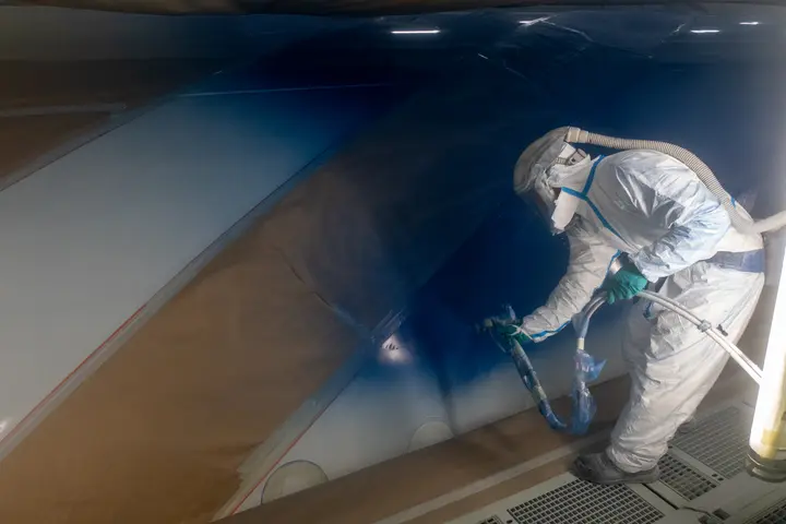 A Delta employee paints the body of an aircraft for Delta's Centennial livery.