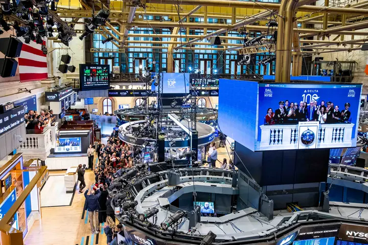 Overhead shot of NYSE floor with main screen displaying Ed and Delta people ringing the bell.