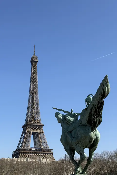 A bronze statue of the winged horse Pegasus is in the foreground, with the Eiffel Tower prominent in the background under a blue sky, viewed from the Pont de Bir-Hakeim.