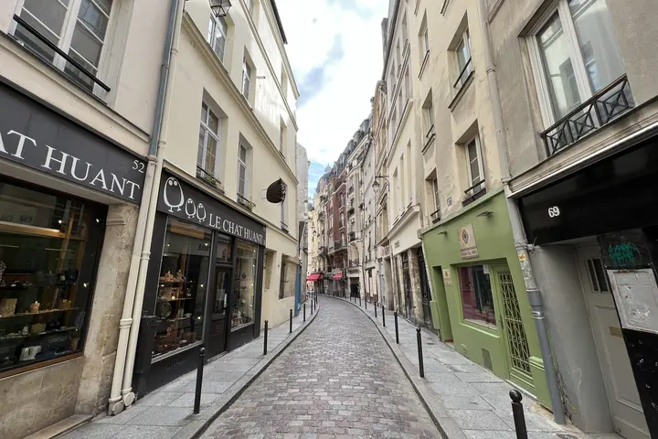 Narrow cobblestone street lined with small boutiques and pastel buildings in a historic Paris neighborhood.