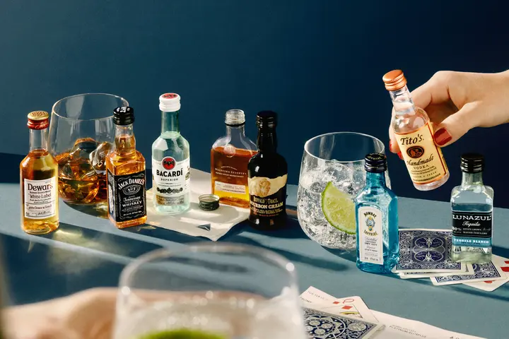 A lineup of airplane bottles of alcohol against a blue background