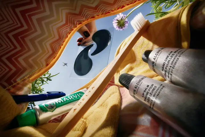 View inside a Missoni amenity kit showing a toothbrush, toothpaste, lip balm, hand cream, eye mask, and pen against a blue sky.