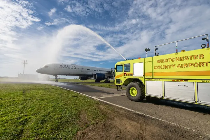 Delta airplane receives water salute from airport fire truck on runway.
