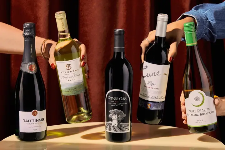 Hands reaching for a selection of sparkling, red and white wine bottles displayed on a table.
