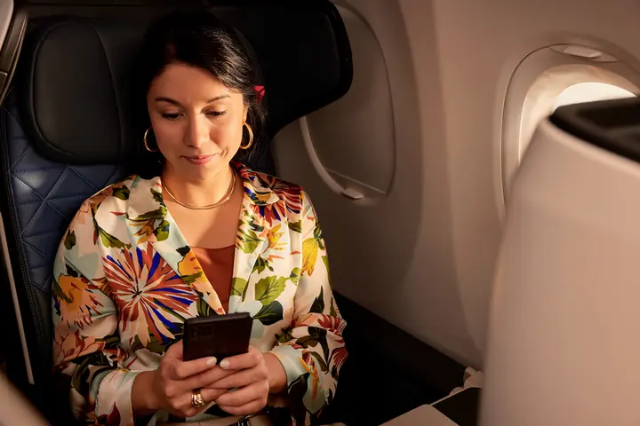 A customer seated on a Delta plane uses their mobile device.