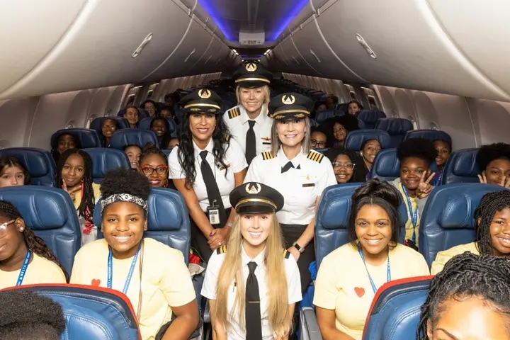 The girls selected for Delta's WING Flight 2023 pose with Delta pilots on the plane.