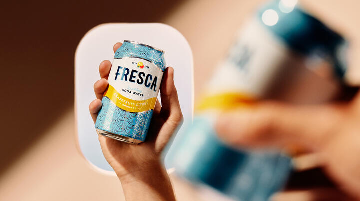 Hand holding a chilled Fresca grapefruit citrus soda can, with an airplane window softly blurred in the background.