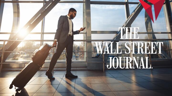 Traveler in a suit walks through a sunlit airport terminal, pulling a rolling suitcase and looking at a phone, with “The Wall Street Journal” text overlaid.