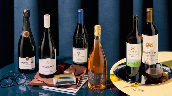Assortment of wine bottles arranged with travel accessories, a glass of wine and decorative props.
