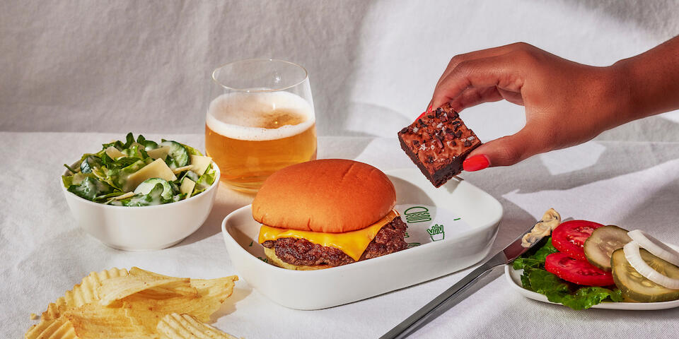 A Shake Shack burger with a side of chips, a salad, and burger fixings.