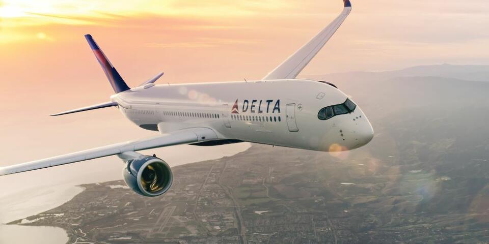 Delta aircraft flying above a coastal city with sun setting in background