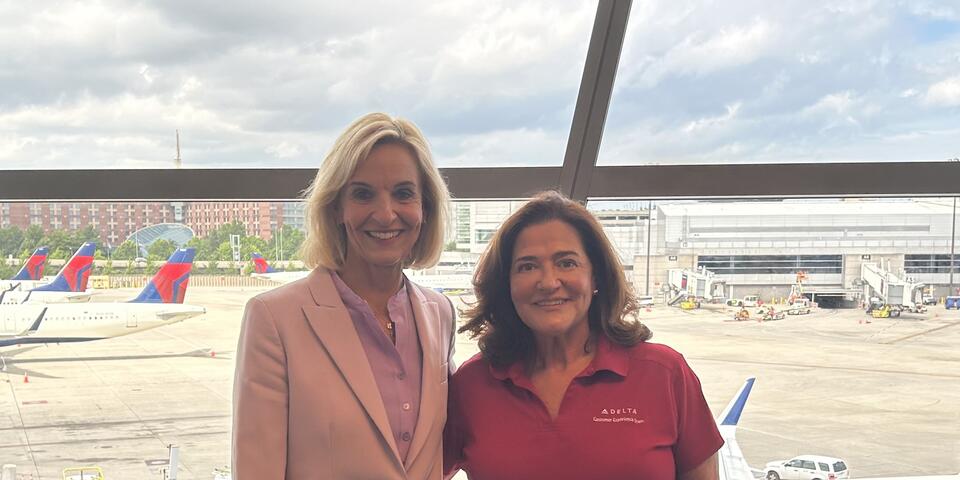 Delta employees Allison Ausband and Nancy Cohn posing against a backdrop of the Boston airport ramp.