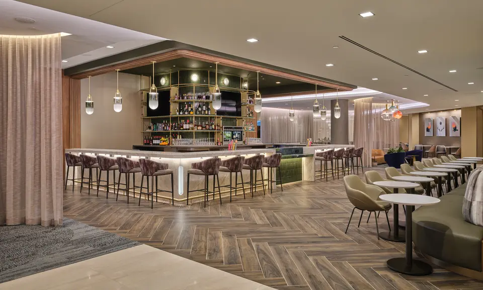 Lounge bar with high‑back stools, illuminated shelving, warm lighting and adjacent seating areas with small tables