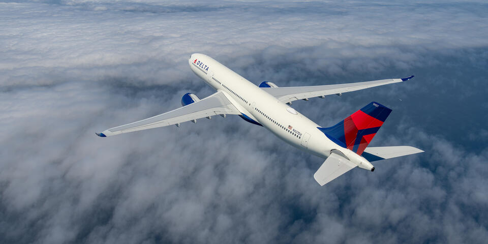 A Delta Air Lines A330-900 flies over clouds.