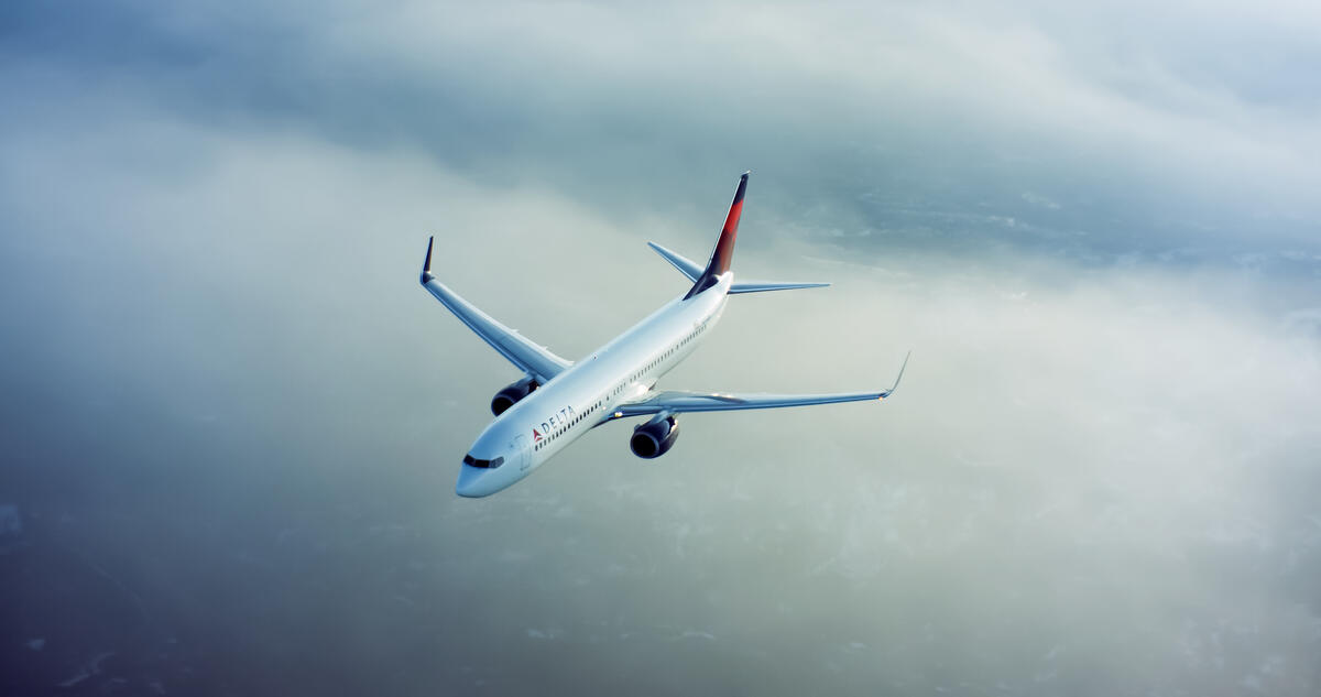A 737-900 flies through clouds with a cityscape underneath.