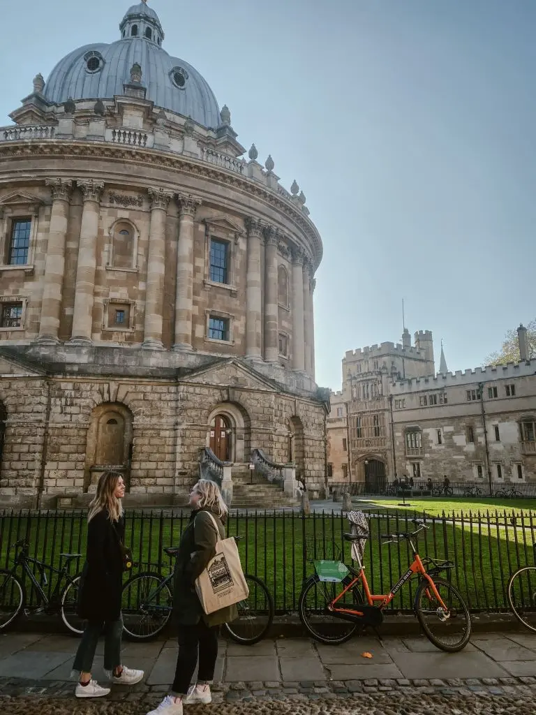 Two people stand in front of the Radcliffe Camera building at the University of Oxford.