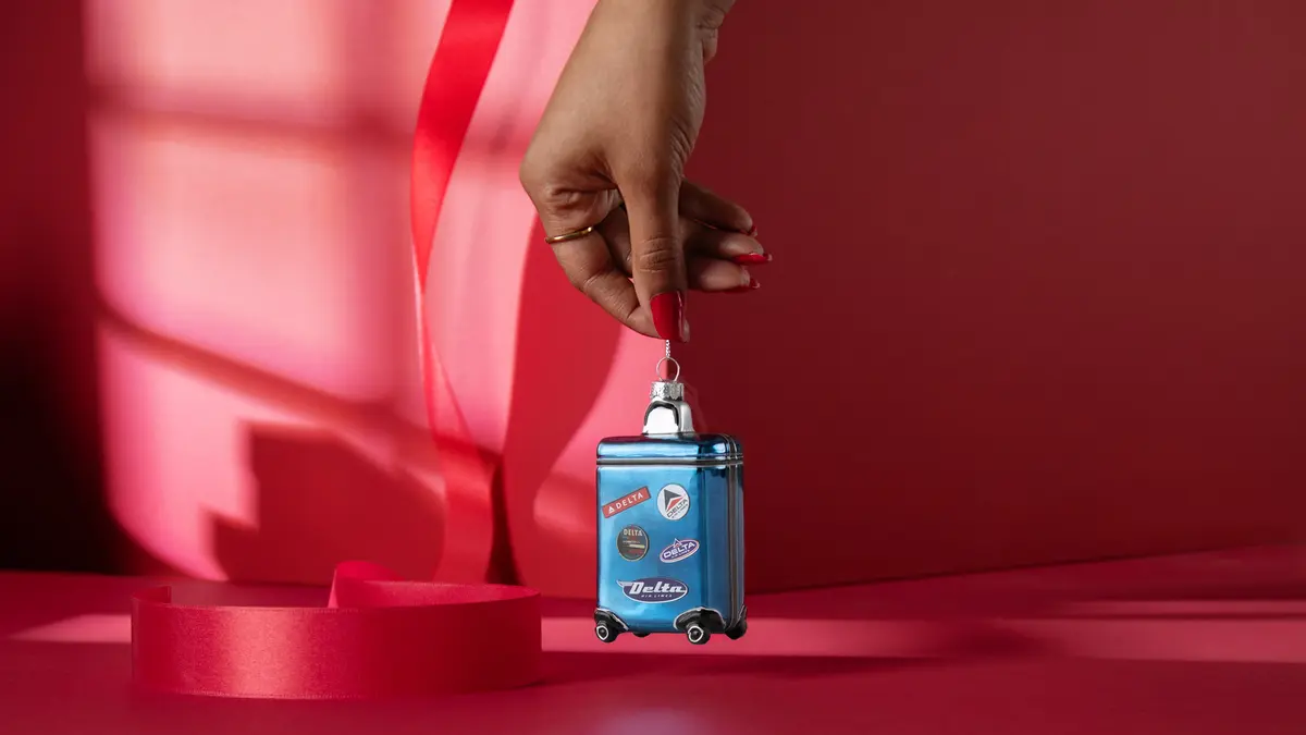Roll into the holidays with our glass, Heritage Delta Suitcase ornament. This ornament is guaranteed to standout on your tree with its blue hues and miniature Heritage patches.  