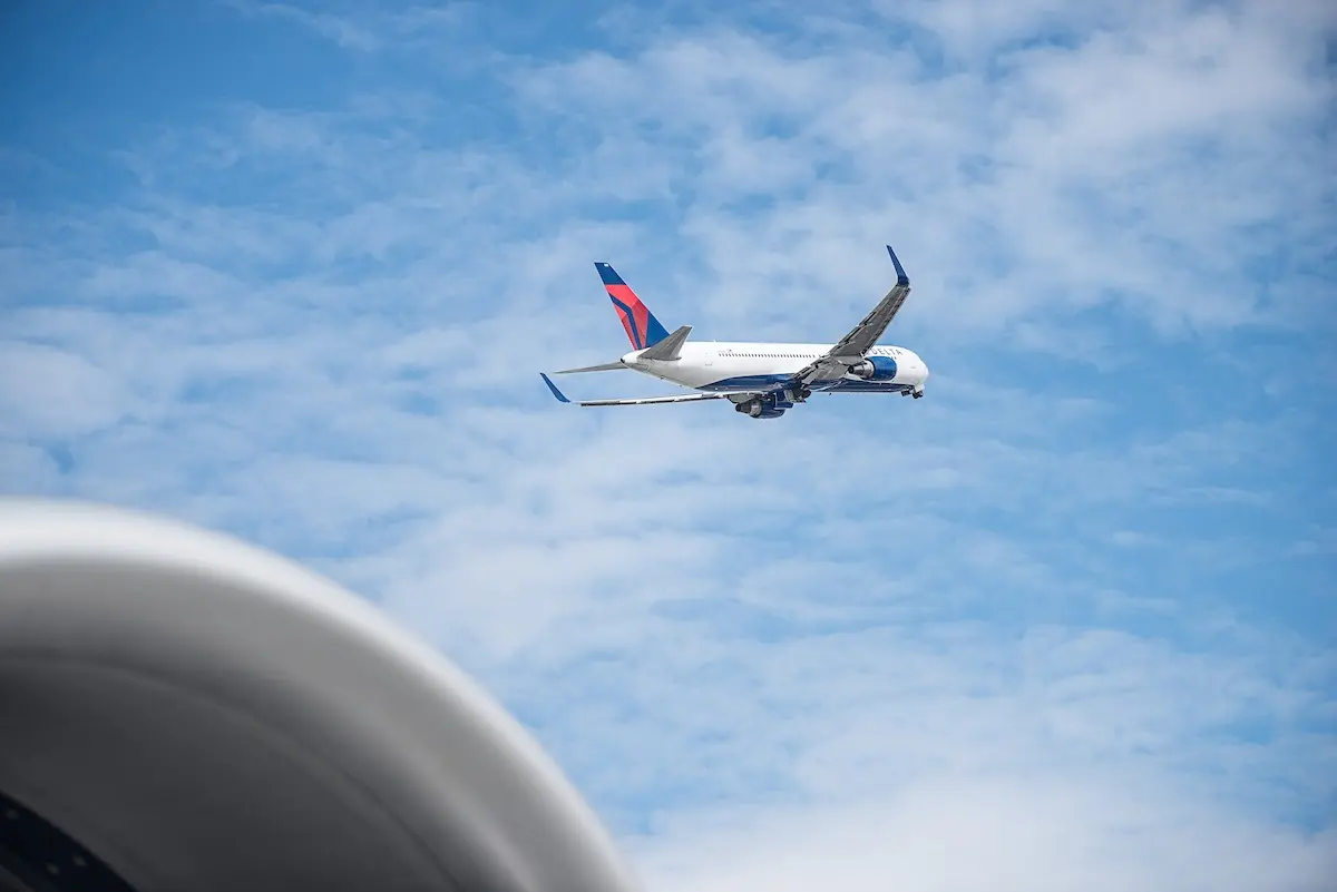 Delta 767 aircraft shortly after takeoff with blue sky and clouds in background