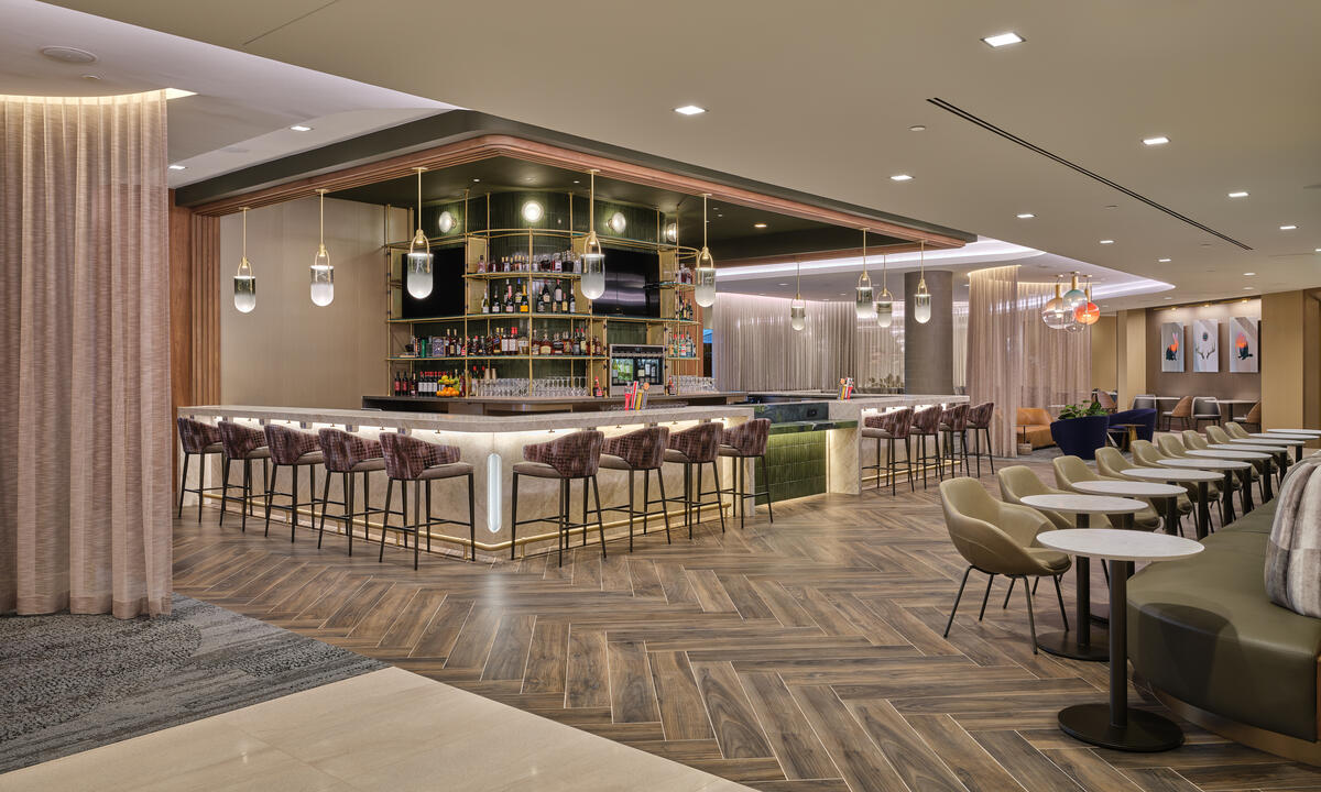 Lounge bar with high‑back stools, illuminated shelving, warm lighting and adjacent seating areas with small tables