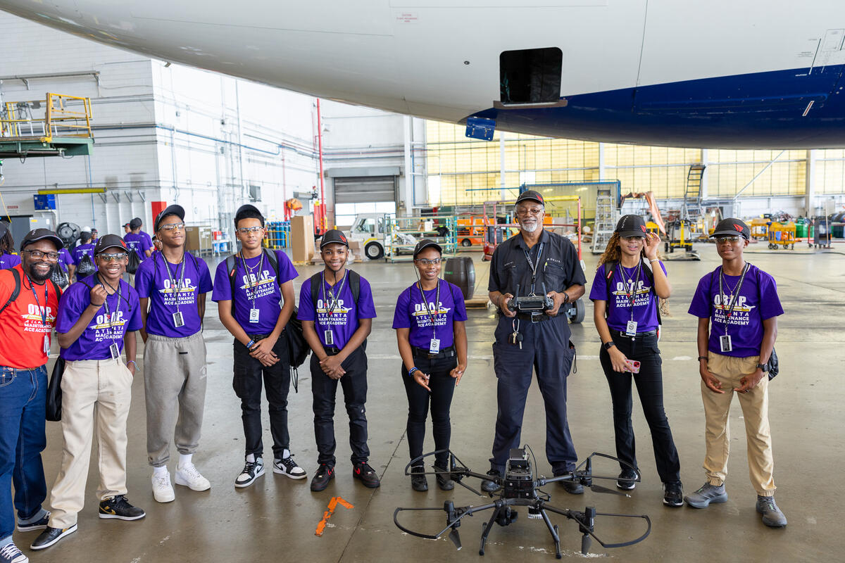 ACE Academy students and a Delta employee stand in an aircraft maintenance hangar beside a large drone during a hands-on learning session.