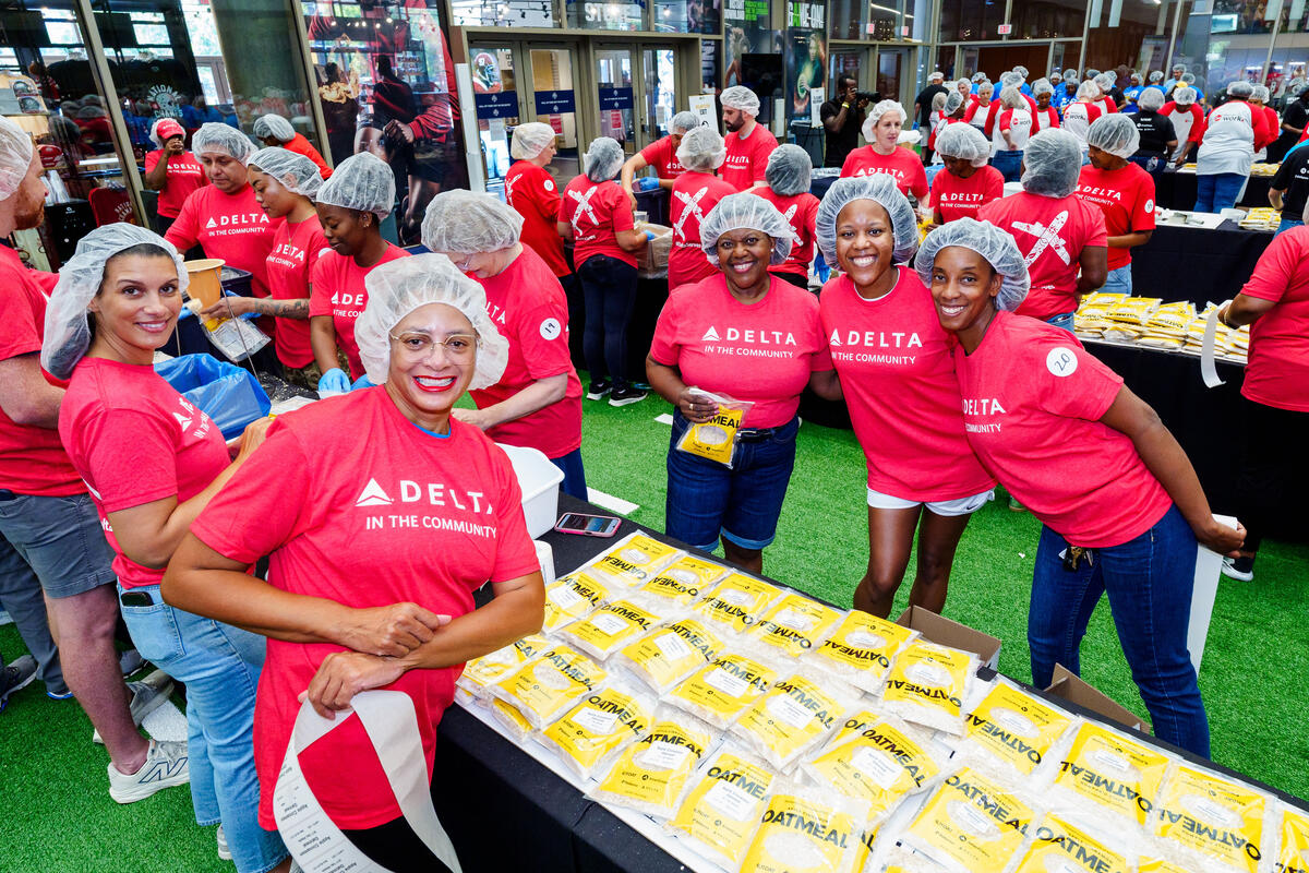 Delta employees wearing red "Delta in the Community" shirts and hairnets assemble meal kits during a volunteer service event.