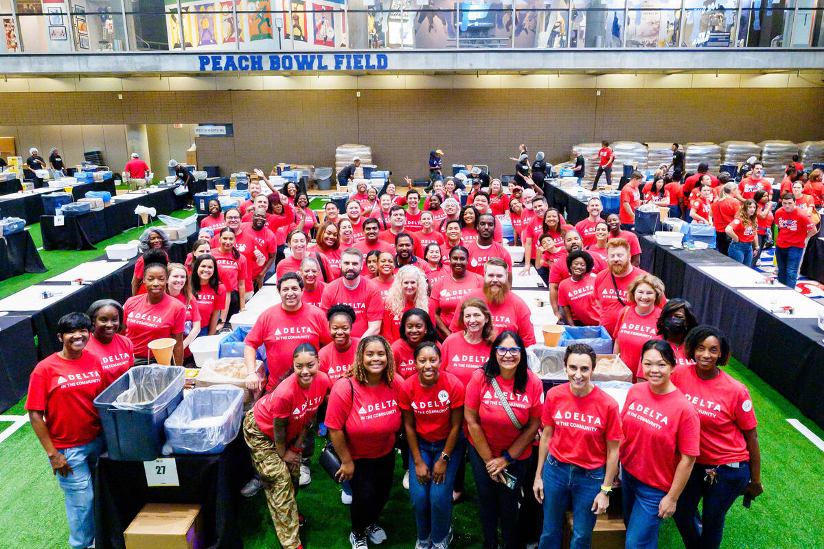 Large group of Delta volunteers in red “Delta in the Community” shirts pose for a photo on Peach Bowl Field during a community service event.