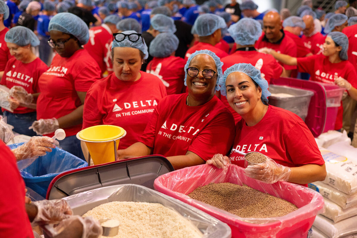 Delta volunteers in red shirts, gloves, and hairnets scoop ingredients and assemble