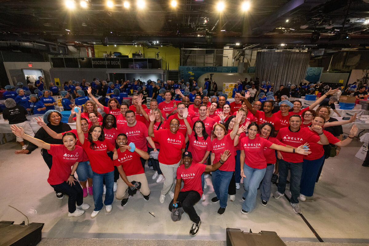 Delta employees and customers gather for a volunteer event, posing for a group photo while assembling meals in support of 9/11 Day service activities.